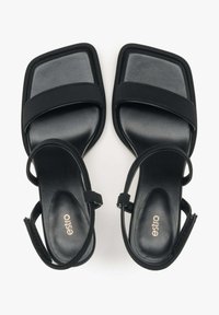 Zwarte hoge hak sandalen met een vierkante teenontwerp, twee centrale bandjes en een verstelbare enkelband. Gladde leren textuur met minimale hardware.