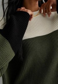 Maglione a maglia con un design a blocchi di colore che presenta sezioni nere, crema e verde oliva; tessuto testurizzato, maniche a costine e scollo rotondo.