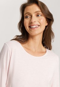 Vaaleanpunainen pitkähihaisen paita, jossa on pyöreä kaula-aukko. Kankaan pinta on pehmeä ja siinä on hienovarainen heather-kuviointi sekä rento leikkaus.