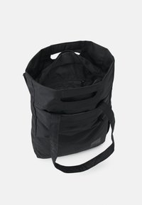 Schwarze Stofftasche mit zwei Griffen, einem offenen Oberteil und einer Reißverschlusstasche im Inneren für sichere Aufbewahrung.