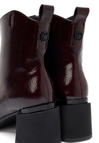 Stivaletti alla caviglia in pelle patinata bordeaux con una finitura testurizzata. Presentano un tacco a blocco e dettagli di cucitura prominenti sul gambale.