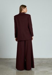 Bordeaux oversized blazer met bijpassende wijde broek, met een gladde textuur en gestructureerd ontwerp, gezien vanuit de achterkant.