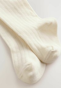 Chaussettes côtelées de couleur crème avec une texture douce et un bout arrondi, présentant un design simple et minimaliste.