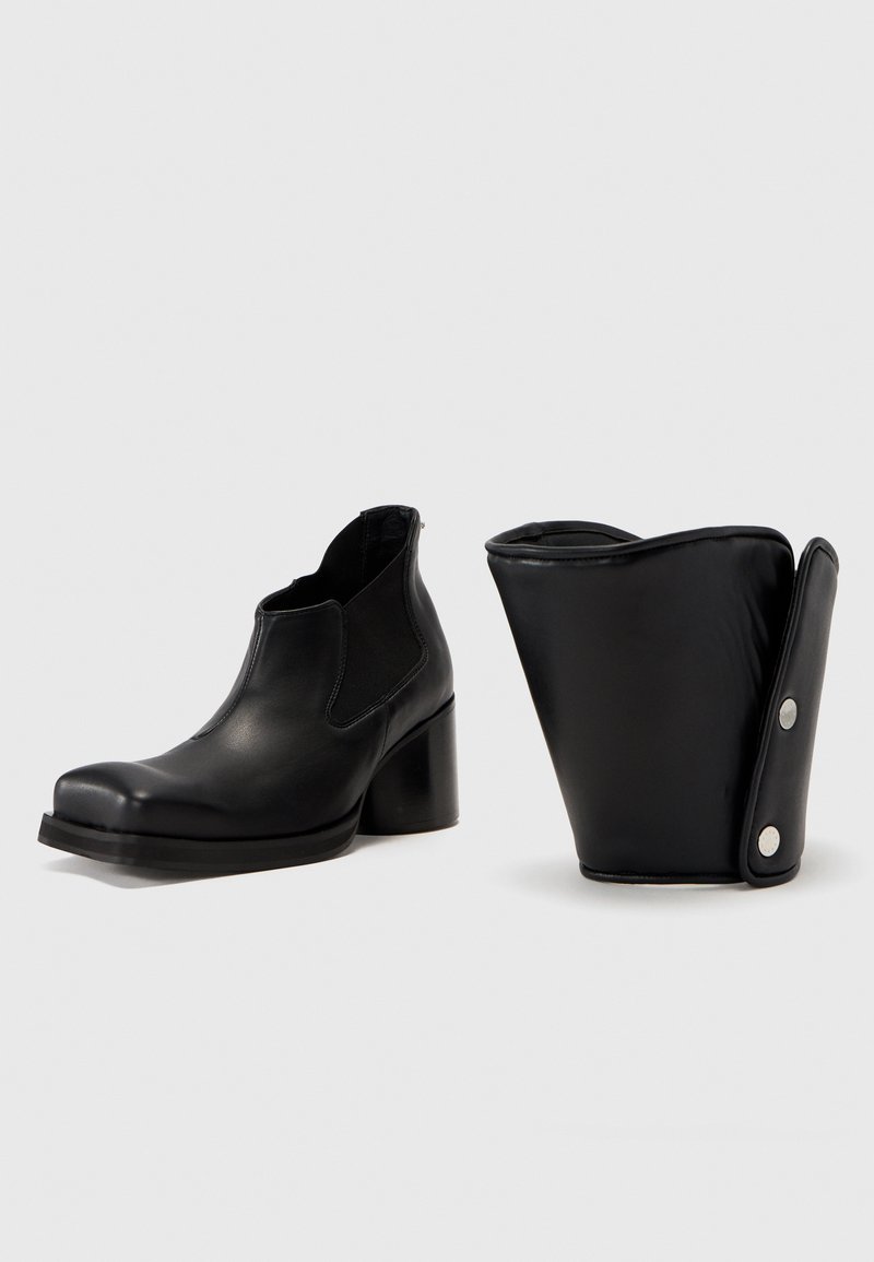 Zwarte leren enkelboots met een blokhak, voorzien van elastische zijkanten en een ronde neus. Inclusief een afneembare, gemusterde manchetaccessoire.