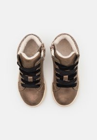 Metalické bronzové vysoké tenisky s černými šňůrkami, kožešinovou podšívkou a bočním zipem. Textura je hladká s lesklým povrchem.