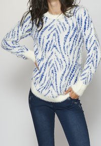 Fluffy white sweater with blue zigzag pattern, features a round neckline, long sleeves, and soft textured cuffs and hem.