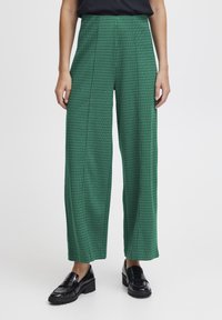 Pantaloni a gamba larga verde a scacchi realizzati in un tessuto testurizzato, con pieghe frontali e un design a vita alta, abbinati a mocassini neri.