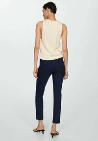 Béžový top bez rukávů v kombinaci s námořnicky modrými přiléhavými kalhotami. Top má ribbovanou strukturu, zatímco kalhoty mají hladký povrch a slim fit.