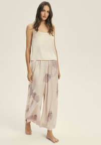 Kremowa satynowa koszulka na ramiączkach z cienkimi paskami w połączeniu z jasnoróżowymi spodniami o szerokich nogawkach, które mają kwiatowy wzór w odcieniach lawendy i szarości.
