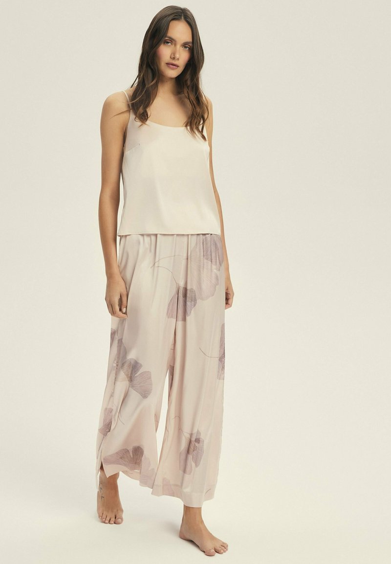 Kremowa satynowa koszulka na ramiączkach z cienkimi paskami w połączeniu z jasnoróżowymi spodniami o szerokich nogawkach, które mają kwiatowy wzór w odcieniach lawendy i szarości.