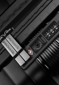 Acercamiento a la cremallera de una maleta negra con tiradores plateados de la marca Pactastic y una cerradura de combinación TSA007 configurada en 000.