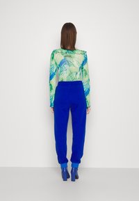 Sheer green top with blue floral pattern and ruffled edges, paired with blue sweatpants and blue heeled ankle boots.