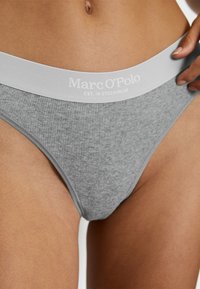 String gris à côtes avec une large ceinture élastique blanche arborant le logo "Marc O'Polo". Axé sur la simplicité et le confort.