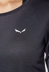 Czarna sportowa koszulka z szerokim dekoltem, wykonana z gładkiego materiału. Posiada biały logotyp na obszarze klatki piersiowej.