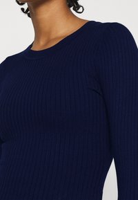 Granatowy sweter z prążkowanego dzianiny o okrągłym dekolcie i długich rękawach, charakteryzujący się miękką fakturą i poziomymi liniami na całej tkaninie.