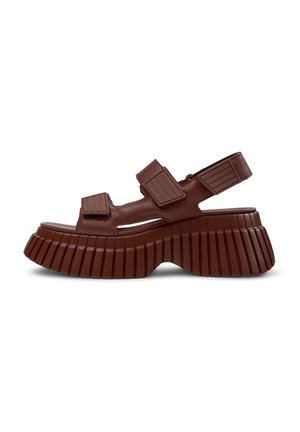 Brown leather sandals featuring adjustable straps, a chunky ridged sole, and an open toe design. Substantial texture on the sole and straps.