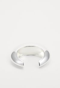 Brazalete de metal plateado con una superficie lisa y brillante y extremos redondeados, que presenta un diseño abierto y una forma elegante y moderna.