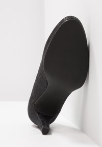 Chaussure à talon haut en tissu tissé noir avec un dessus texturé, un bout pointu et une semelle en caoutchouc, affichant la taille 37 sur la semelle.