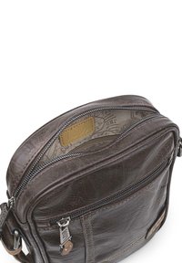 Bolso cruzado de cuero marrón con apertura con cremallera, parche con logo y costuras en contraste. Presenta un acabado texturizado y un patrón interior.