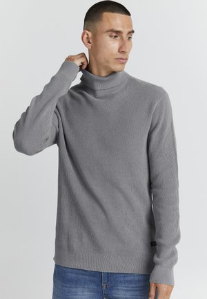 Grijze turtleneck trui met geribbelde textuur, lange mouwen en een aansluitend ontwerp, gecombineerd met blauwe spijkerbroek.