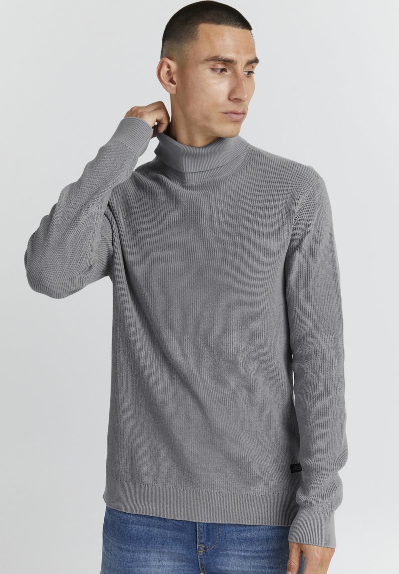 Grå rullekragegenser med ribbestruktur, lange ermer og slim-fit design, parret med blå denimjeans.