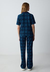 Camicia a maniche corte a motivi argyle blu e verde abbinata a pantaloni coordinati. Entrambi realizzati in tessuto testurizzato con una vestibilità comoda.