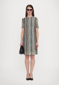 Rochie cu mâneci scurte, cu dungi verticale multicolore, până la genunchi, realizată dintr-un material texturat. Purând o geantă și pantofi negri.