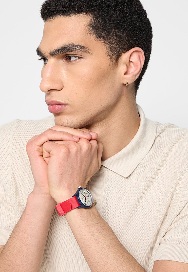 Reloj con correa de goma roja, caja azul marino y esfera blanca. Cuenta con marcadores de hora, tres subesferas y un fondo texturizado.