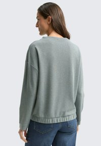 Light green knit sweater with a textured pattern, loose fit, round neckline, and ribbed hem. Paired with blue jeans.