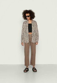 Camisa com padrão de zebra em preto e bege, top cropped preto, calças largas castanhas e sandálias pretas. Usado por uma pessoa com cabelo encaracolado e óculos de sol.