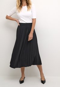 Czarna plisowana spódnica midi z lejącego materiału z elastycznym pasem. W zestawie z dopasowaną białą koszulką z krótkim rękawem i czarnymi, spiczastymi balerinami.