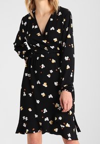 Černé zavinovací šaty s dlouhými rukávy, zdobené květinovým vzorem v bílé, žluté a oranžové barvě. Rukávy s volánkovým lemem a detail pružného pasu.