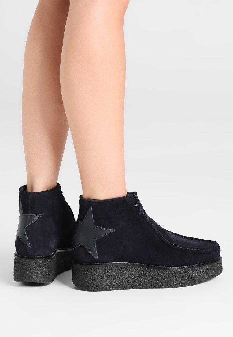 Bottines en daim bleu marine foncé avec une semelle plateforme noire texturée, ornées d'un accent étoile proéminent sur le côté extérieur.
