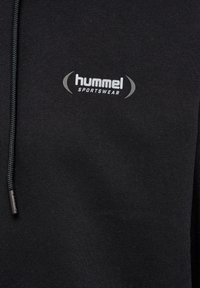 Zwart sportstof met wit "hummel SPORTSWEAR" logo en een deel van een zwarte trekkoord zichtbaar aan de linkerkant.