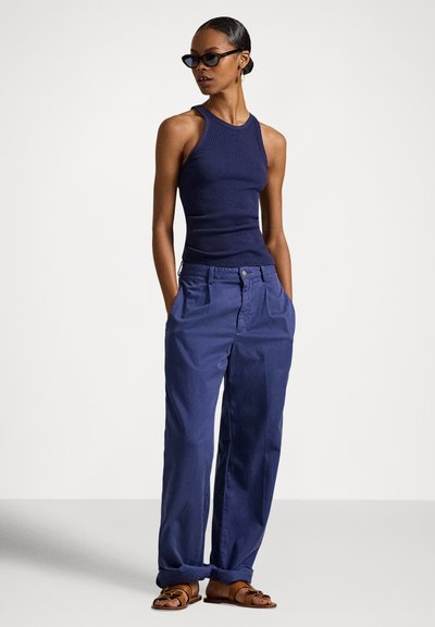 Granatowy prążkowany top na ramiączkach w połączeniu z luźnymi granatowymi spodniami. Stylizację dopełniają sandały i eleganckie, ciemne okulary przeciwsłoneczne. Prosty krój, minimalne detale.