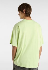 Camiseta de algodón verde claro con cuello redondo, mangas cortas y un corte relajado. La vista trasera muestra un diseño sencillo sin gráficos ni patrones.