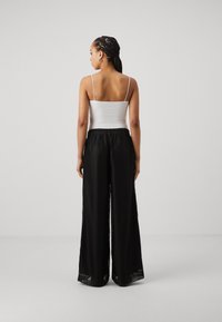 Sorte vide bukser med et struktureret mønster, elastisk talje, parret med en tætsiddende hvid tanktop, vist fra ryggen.