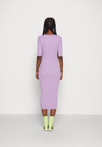 Robe en tricot côtelé lilas avec manches courtes, silhouette ajustée et ourlet jusqu'aux genoux; portée avec des bottines vertes brillantes.