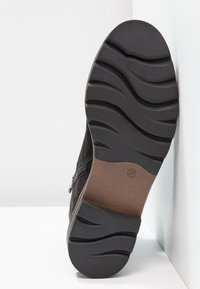 Chaussure noire avec une semelle en caoutchouc texturée présentant des rainures courbes, une fermeture éclair latérale et une semelle intérieure marron. Taille indiquée : 37.