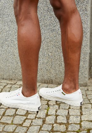 Baskets en toile blanches avec semelle en caoutchouc texturé, présentant des lacets ronds, un logo sur le talon et des accents contrastants près de la languette.
