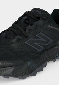 Μαύρο αθλητικό παπούτσι New Balance με υφασμάτινο πλέγμα, παχιά σόλα, κλείσιμο με κορδόνια και λογότυπο στο πλάι και στη γλώσσα.