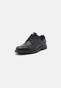 Chaussure habillée pour homme en cuir noir à lacets, bout arrondi, talon bas et col rembourré sur fond blanc.