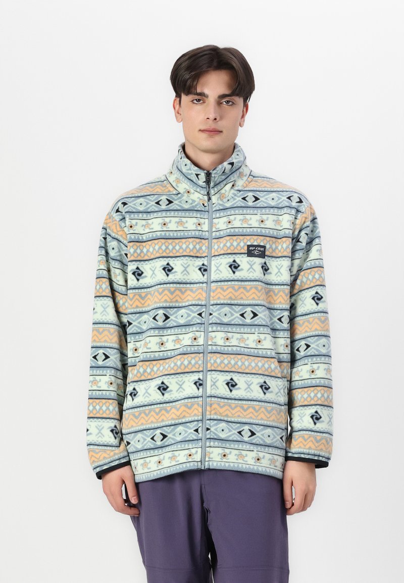 Veste en polaire présentant un motif géométrique multicolore en bleu, orange et crème, avec un col montant et une fermeture éclair. Texture douce.