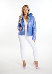 Giacca puffer viola chiaro con finitura lucida, chiusura con zip e cappuccio staccabile; abbinata a jeans skinny bianchi e tacchi coordinati.