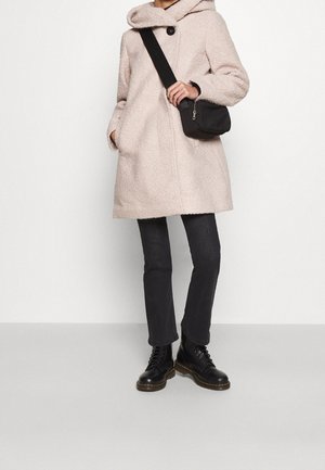 Abrigo texturizado rosa claro con capucha, cierre de botón negro, combinado con jeans oscuros y botas negras con cordones, y un pequeño bolso cruzado negro.