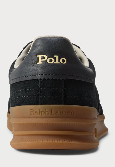 Adidași din suede și piele negri, cu o talpă din cauciuc bej, cu un brand "Polo" auriu și detalii cusute pe călcâi.