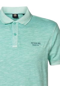 Světle tyrkysová polokošile s texturovaným vzorem. Má límeček, dvě knoflíky a vyšitý nápis "PETROL IND. HAWAII U.S.A."