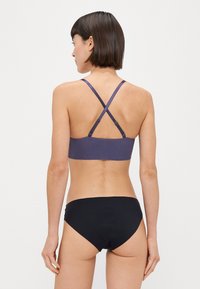 Top bikini a righe viola con design incrociato sul retro, abbinato a slip bikini neri a tinta unita. Il materiale sembra liscio e aderente.