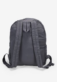 Mochila gris con tejido acolchado, correas dobles para los hombros y un asa superior. Contiene bolsillos laterales y un compartimento principal con cremallera.