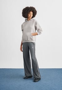 Γκρι φούτερ με κουκούλα και μπροστινή τσέπη, σε συνδυασμό με γκρι αθλητικό παντελόνι με λευκές ρίγες και μικρό λογότυπο, υφασμάτινη υφή.